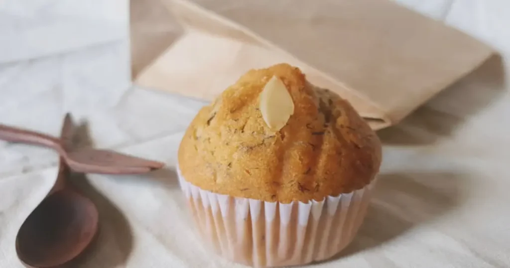 Freshly baked banana muffins arranged on a wooden tray, golden-brown and fluffy, with a broken muffin showing its moist texture. Surrounded by ripe bananas, a bowl of flour, and walnuts, highlighting the homemade feel. Text overlay reads: 'Simple Banana Muffin Recipe: Ready in Just 30 Minutes.' Blog domain bananarecipess.com is displayed in the footer.